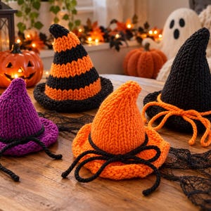 May include: Three knitted witch hats in purple, orange, and black. The purple hat has a black cord, the orange hat has a black cord, and the black hat has an orange cord. The hats feature a pointed crown and a wide brim, crafted with a chunky knit texture.