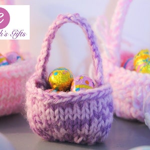 May include: Three small knitted baskets filled with chocolate Easter eggs. The baskets are pink and purple and have a woven texture. The eggs are wrapped in foil and have a variety of colors and designs.