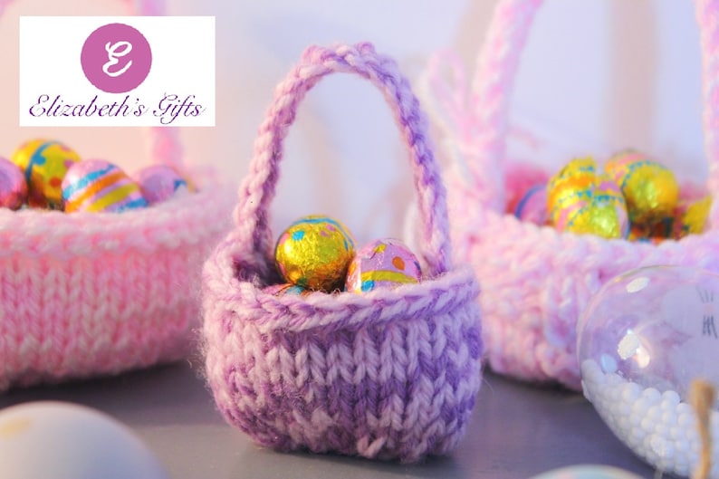 May include: Three small knitted baskets filled with chocolate Easter eggs. The baskets are pink and purple and have a woven texture. The eggs are wrapped in foil and have a variety of colors and designs.