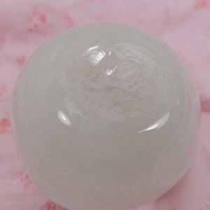 May include: A white, round, smooth, translucent sphere with a slight pink hue. The sphere is sitting on a pink surface.