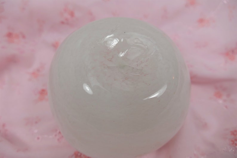 May include: A white, round, smooth, translucent sphere with a slight pink hue. The sphere is sitting on a pink surface.