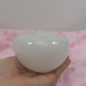 May include: A white, apple-shaped candle on a pink floral background.