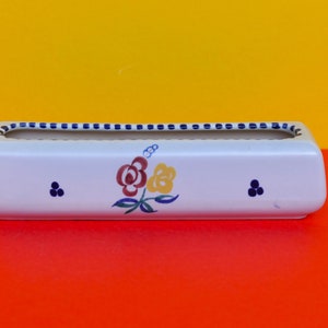 May include: White ceramic planter with a blue and white trim and a floral design featuring red, yellow, and blue flowers.