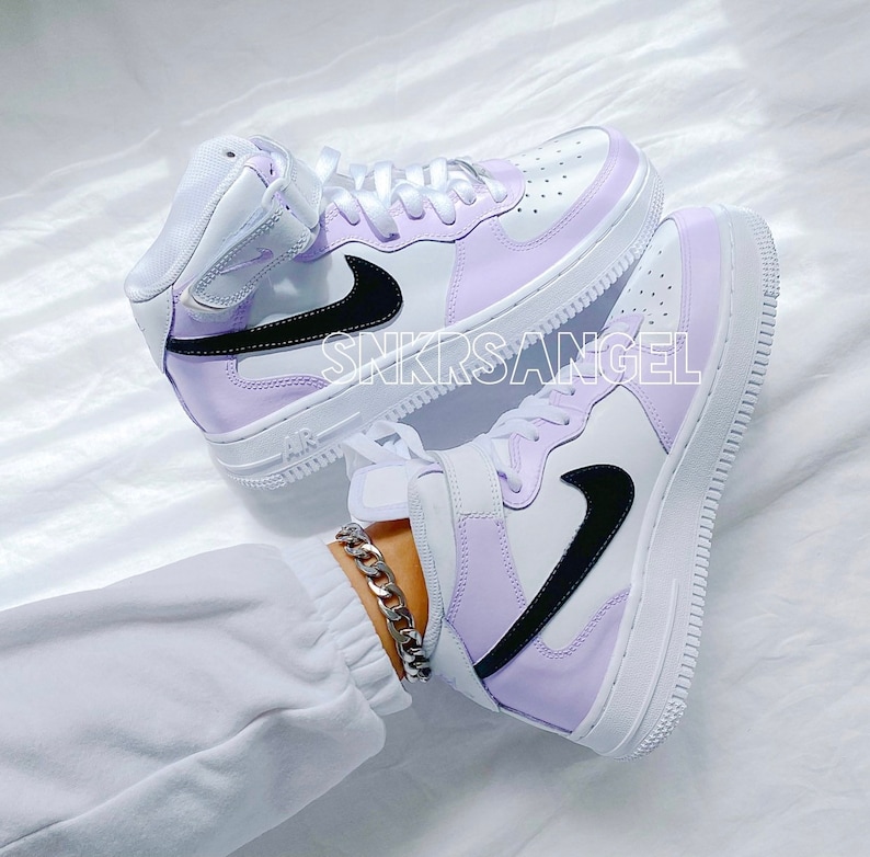 Op de afbeelding: Een paar witte high-top sneakers met een lavendel en zwart kleurenblokontwerp. De sneakers hebben een zwart swoosh-logo en een witte zool.