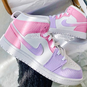 May include: A pair of white high-top trainers with a pink and purple colour block design. The trainers have a white swoosh logo on the side and a pink and purple swoosh logo on the back.