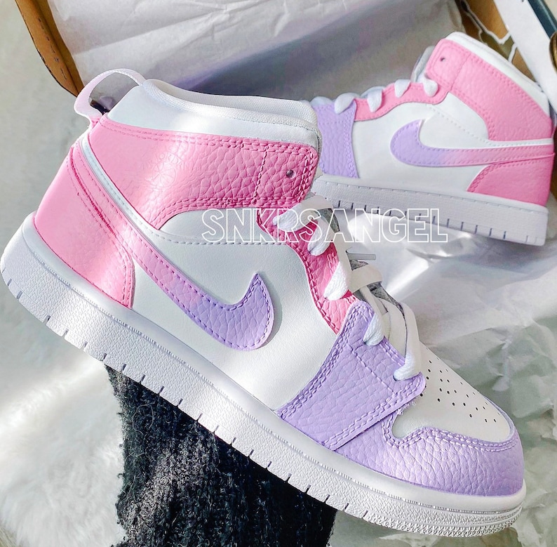 May include: A pair of white high-top trainers with a pink and purple colour block design. The trainers have a white swoosh logo on the side and a pink and purple swoosh logo on the back.