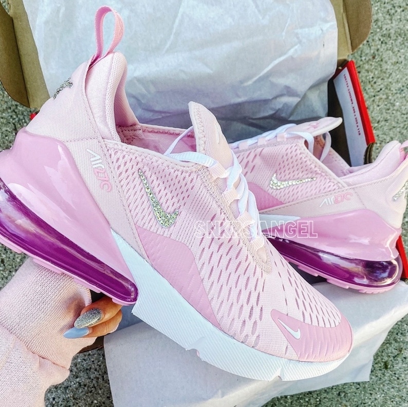 May include: Pink Nike Air Max 270 trainers with a white swoosh and a clear crystal embellishment. The trainers have a white midsole and a purple outsole.