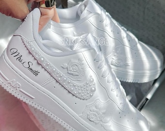 May include: White Air Force 1 sneakers customized with pearl accents and rose details. The text "Mrs. Smith" is displayed on the side. The sneakers are in a box.