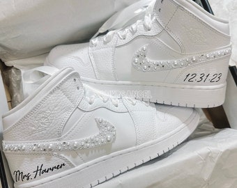 May include: A pair of white high-top sneakers with pearl embellishments on the swoosh and laces. The sneakers are personalized with the text "Mrs. Harren" on one shoe and "12.31.23" on the other.