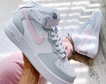 May include: White and gray high-top sneakers with a pink Nike swoosh. The sneakers have a white midsole and a gray outsole. The text "AIR" is visible on the side of the shoe.