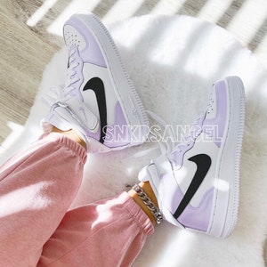 Op de afbeelding: Een paar witte high-top sneakers met een lavendel en zwart kleurenschema. De sneakers hebben een zwart swoosh-logo en een witte tussenzool. De tekst "SNKRSANGEL" is zichtbaar aan de zijkant van de sneakers.