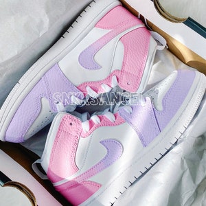 May include: A pair of white, pink and purple high-top trainers with a Nike swoosh logo. The trainers are in a shoebox.