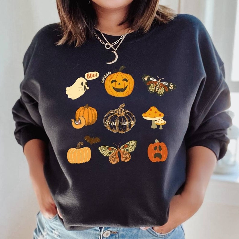 Może przedstawiać: Czarny sweter z motywem Halloween z dyniami, duchem, nietoperzem, motylami i grzybami. Tekst na swetrze brzmi "Boo!" i "Little Pumpkins".