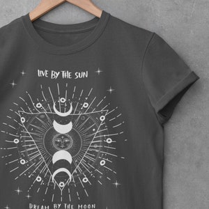 May include: A dark gray t-shirt with a white graphic design featuring a sun and moon with the text "Live by the sun, Dream by the moon".