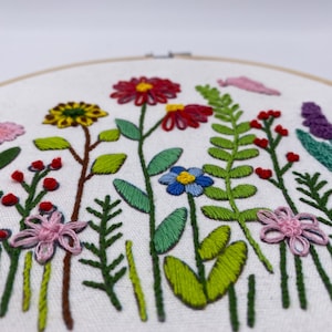 May include: Embroidered hoop art featuring a colourful floral design with pink, red, yellow, blue, and green flowers and leaves.