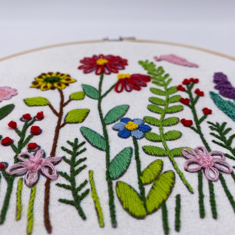 May include: Embroidered hoop art featuring a colourful floral design with pink, red, yellow, blue, and green flowers and leaves.