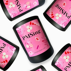 May include: Black cylindrical containers with pink labels featuring the text "PMSing" and various illustrations related to menstruation. The labels also include the website address ANGSTYADDIE.COM. The containers are arranged on a white background.