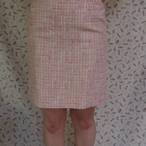 May include: A pink and white tweed skirt with a straight cut, worn with a white, textured crop top. The skirt features a grid pattern. The outfit is completed with brown ankle boots and white socks.