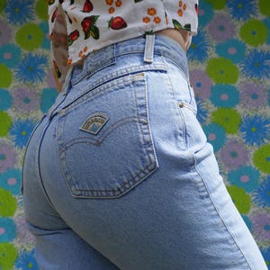 May include: Pale blue denim jeans with a Native Blue label on the back pocket. The jeans are high-waisted and have a classic five-pocket design. A white crop top with a strawberry pattern is also visible.