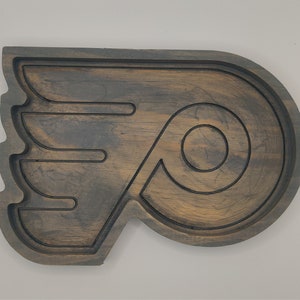 May include: A wooden serving tray shaped like the Philadelphia Flyers hockey team logo. The tray is dark brown with a distressed finish and features a black outline of the logo.