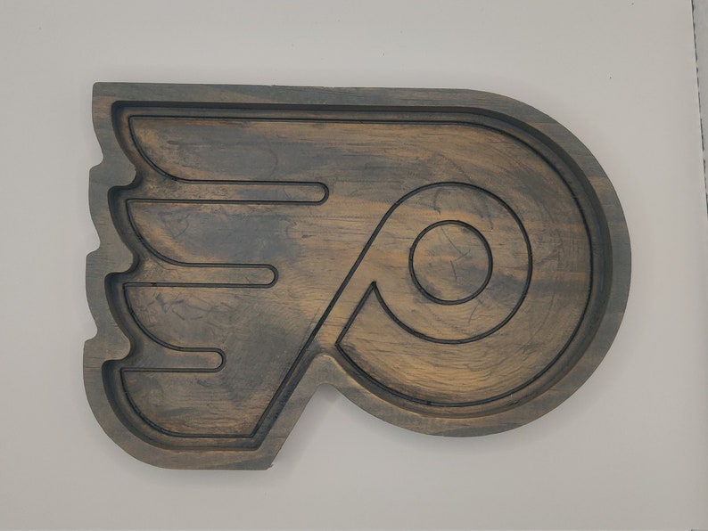 May include: A wooden serving tray shaped like the Philadelphia Flyers hockey team logo. The tray is dark brown with a distressed finish and features a black outline of the logo.