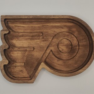 May include: A wooden serving tray shaped like the Philadelphia Flyers hockey team logo. The tray is brown and has a raised design of the team's logo.