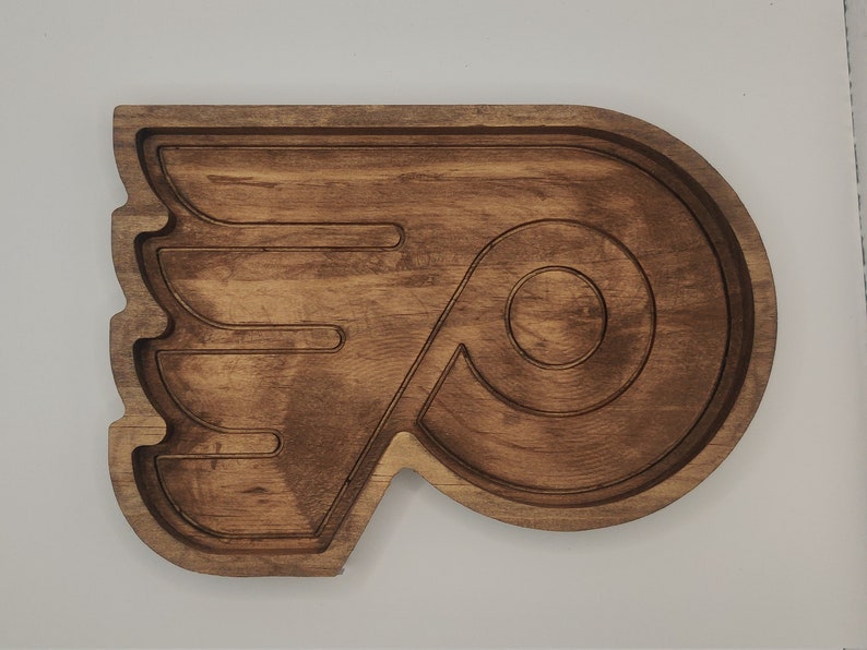 May include: A wooden serving tray shaped like the Philadelphia Flyers hockey team logo. The tray is brown and has a raised design of the team's logo.
