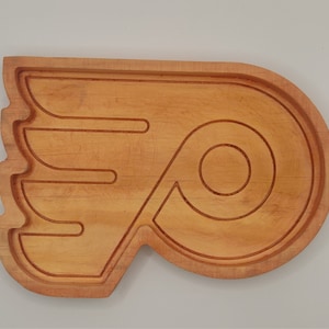 May include: A wooden serving tray shaped like the Philadelphia Flyers hockey team logo. The tray is made of light brown wood and has a natural finish.