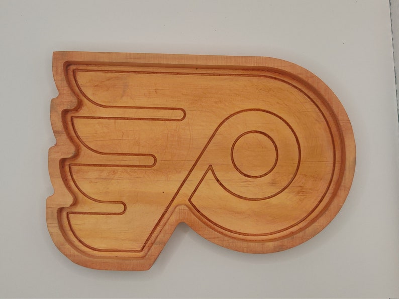 May include: A wooden serving tray shaped like the Philadelphia Flyers hockey team logo. The tray is made of light brown wood and has a natural finish.