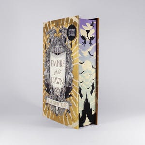 May include: A hardcover book titled "Empire of the Dawn" by Jay Kristoff. The cover is gold with a detailed illustration and the words "Signed by the Author". The spine features a castle silhouette and bats.