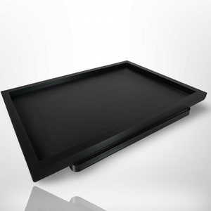 May include: A black rectangular tray with a raised edge. The tray is made of wood and has a smooth finish.