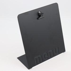 May include: Black metal menu holder with a clip on top. The holder is angled and has the word "menu" embossed on the front.