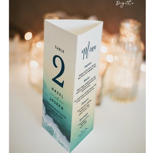 Könnte beinhalten: Eine weiße, dreieckige Hochzeitsmenükarte mit einem Aquarell-Ozean-Design. Die Karte zeigt die Namen "HAZEL und JOSEPH", die Tischnummer 2 und ein Menü mit Vorspeisen, Hauptgerichten, Desserts und Getränken.
