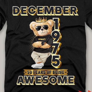 May include: Black t-shirt featuring a cartoon bear wearing sunglasses and a crown, with the text "DECEMBER 1975" and "50 YEARS OF BEING AWESOME." The bear is dressed in a black shirt and white pants. A digital file is available.