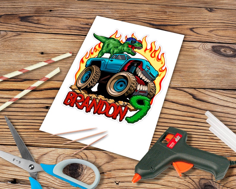 May include: A blue monster truck with flames and a green dinosaur on top. The truck has a toothy grin and the words "BRANDON 9" are written below it.