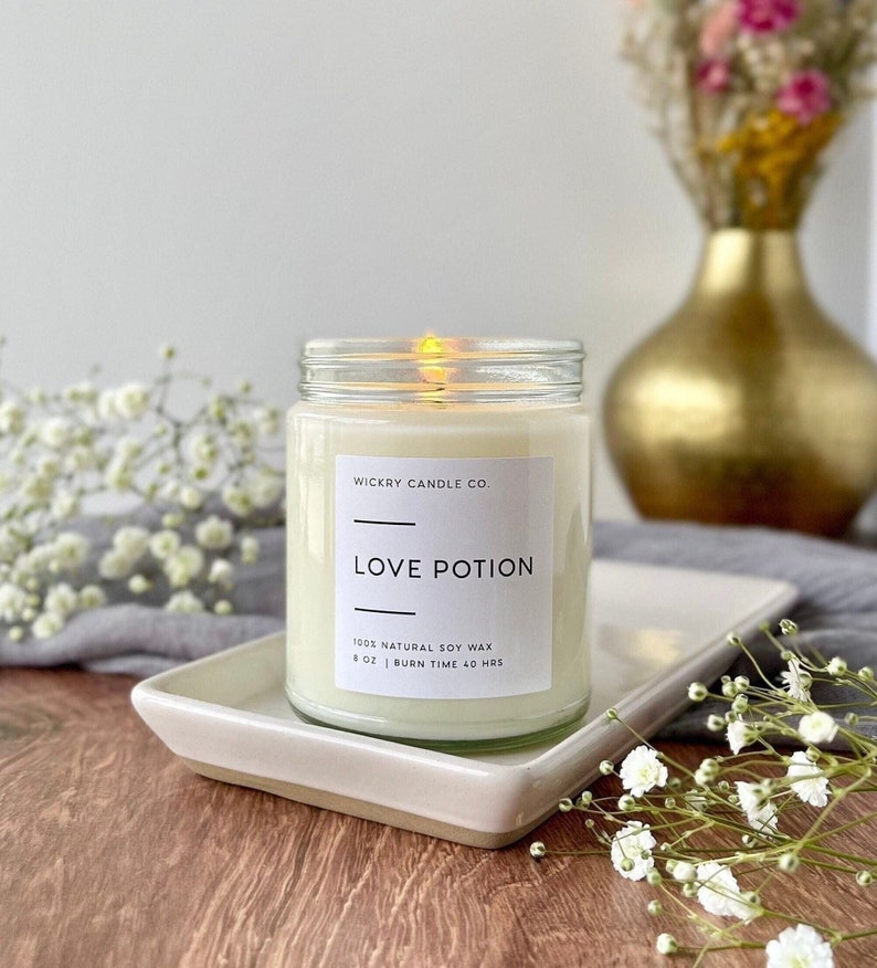 A candle in a clear glass jar with a white label with black text