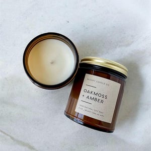 May include: Two amber glass candle jars with black lids. The jar on the right has a label that reads "WICKRY CANDLE CO. OAKMOSS + AMBER 100% NATURAL SOY WAX 8 OZ | BURN TIME 40 HRS".