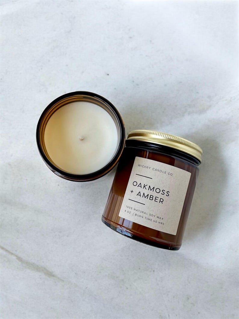 May include: Two amber glass candle jars with black lids. The jar on the right has a label that reads "WICKRY CANDLE CO. OAKMOSS + AMBER 100% NATURAL SOY WAX 8 OZ | BURN TIME 40 HRS".