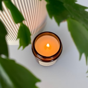 May include: A brown glass candle jar with a white label that reads "Honeysuckle" and a lit candle inside.