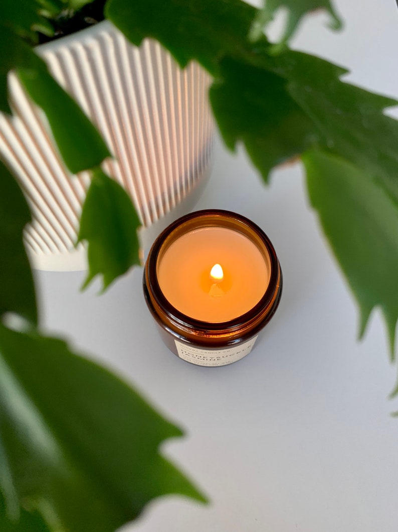 May include: A brown glass candle jar with a white label that reads "Honeysuckle" and a lit candle inside.