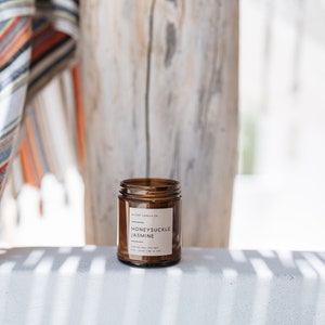 May include: A brown glass candle jar with a white label that reads "Honeysuckle Jasmine" and "Wicary Candle Co.".