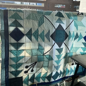 May include: A rectangular quilt featuring a geometric pattern of triangles and diamonds in shades of teal, navy blue, and white. The design includes various fabric textures, including solid colors, small dots, and checkered patterns, with stitched details.