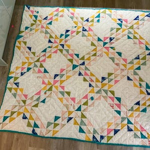 May include: A handmade quilt with a white background and a repeating pattern of colorful triangles. The triangles are in shades of pink, yellow, blue, and green. The quilt has a teal border.