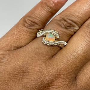 May include: A gold and silver wire wrapped ring with an opal gemstone. The ring is on a person's finger.