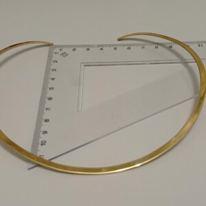 May include: A gold-colored choker necklace, approximately 13 inches in diameter, is displayed on a white surface. The necklace is measured with a clear ruler. The choker has a simple, elegant design.
