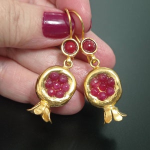 May include: Gold earrings shaped like pomegranates with red gemstone accents.