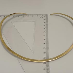 May include: A gold-colored choker necklace with a simple, minimalist design. The necklace is approximately 13 inches in diameter and is measured with a clear ruler. The jewelry is displayed on a white surface.