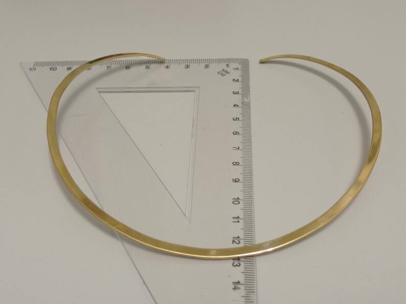 May include: A gold-colored choker necklace with a simple, minimalist design. The necklace is approximately 13 inches in diameter and is measured with a clear ruler. The jewelry is displayed on a white surface.