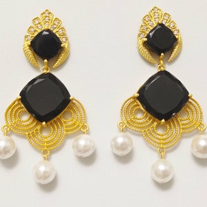 May include: A pair of gold-coloured earrings featuring black square gemstones and white pearl drops. The earrings have a decorative filigree design and are embellished with small clear crystals.