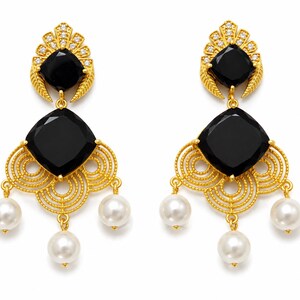 May include: A pair of gold-coloured chandelier earrings featuring black square-cut stones and white pearl drops. The earrings have a decorative filigree design and are adorned with small clear crystals.